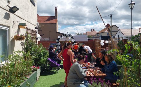 People sitting in a garden, some eating food, others wandering around.